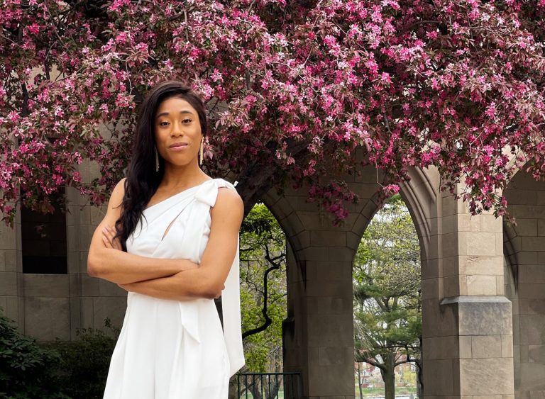 Kaye-Alese Green (LAW'25, MED'25) stands in front of a blooming tree on BU's campus
