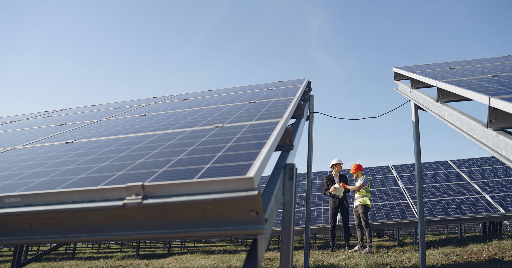 Two people stand in a field of large solar panels.