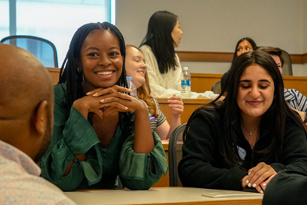 Two female students chat with their classmates in a lecture hall.