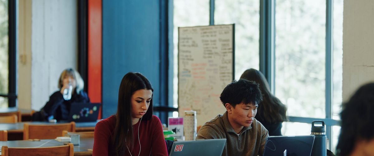 Students working independently at tables next to large windows in Mugar LIbrary
