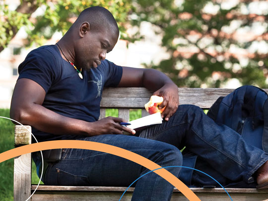 A Boston University student studying and eating an apple on a bench outdoors