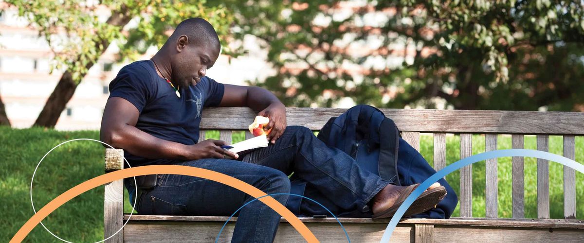 A Boston University student studying and eating an apple on a bench outdoors