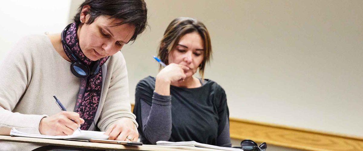 Two students writing notes in a classroom setting