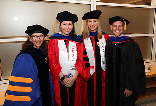 Recent graduates in graduation cap and gown posing for photo