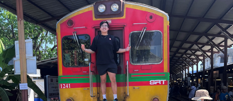 A smiling study abroad student stands on the back of a colorful trolly in Asia
