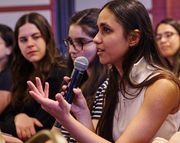 Young woman seated with microphone asking a question to person on stage