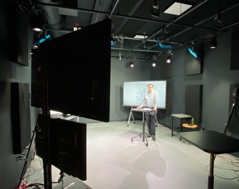 Male professor stands in a studio teaching an online class.