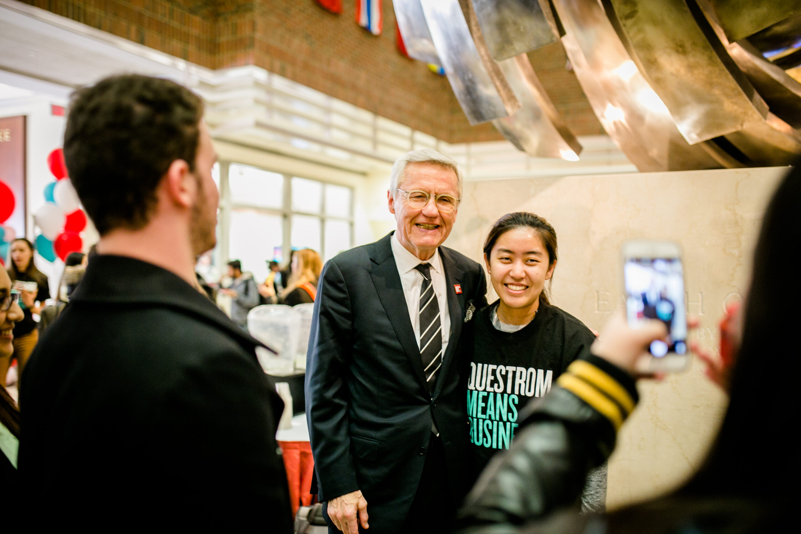 Allen Questrom and student smile for photo in atrium