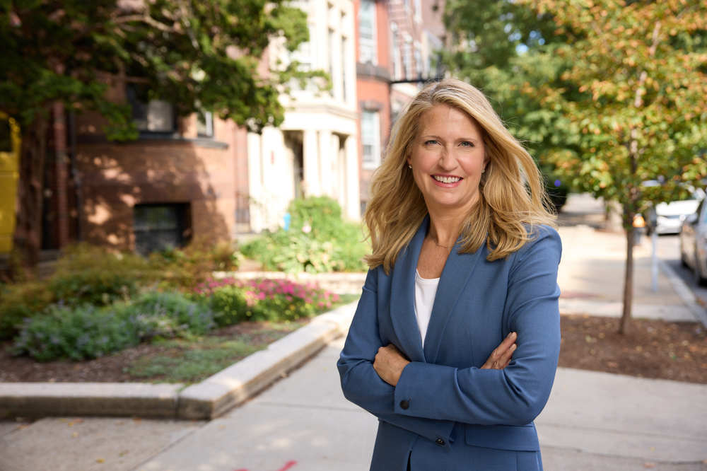 Woman in business suit with arms folded smiling at camera on campus