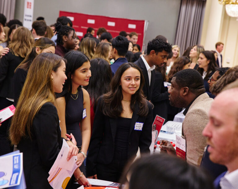Three women undergrads speak with an employer at a crowded networking event