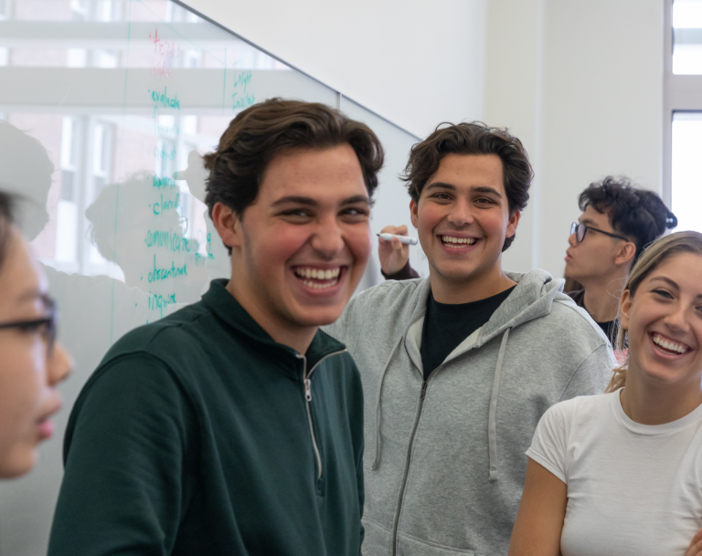 Student group works at the whiteboard and smiles