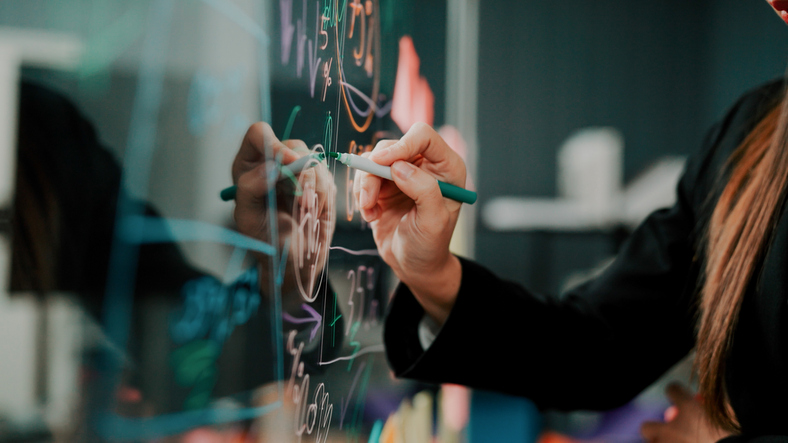 Woman's hand in profile writing on a pane of glass with dry erase marker