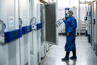 Masked-and-gowned scientist with ultra-cold temperature freezers