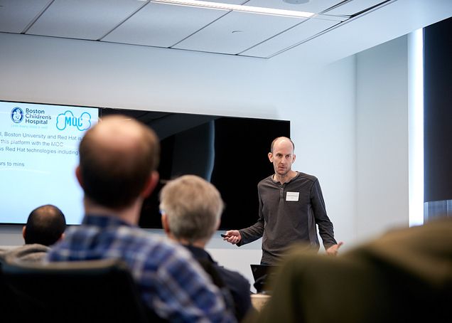 Dan McPherson gives a presentation on ChRIS in the front of a conference room with developers watching around a table.