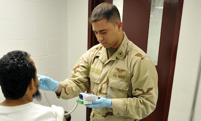 A Navy physician takes the temperature of a Guantanamo detainee.