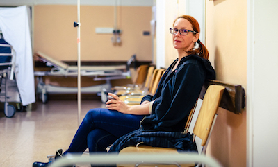 Woman with ponytail and sweatshirt sitting in hospital ward hallway 