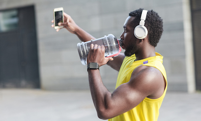Man in workout clothes and headphones takes a selfie while drinking water