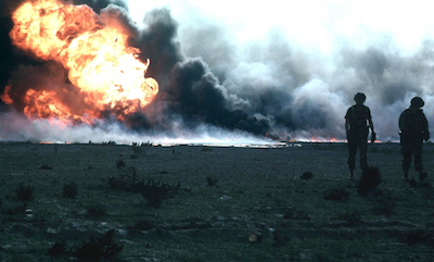 Two soldiers stand in front of a burning oilfield in Kuwait during Operation Desert Storm.