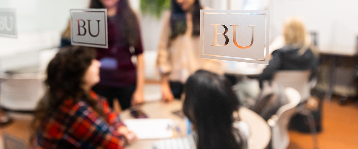 Students gather around a table, blurry behind glass