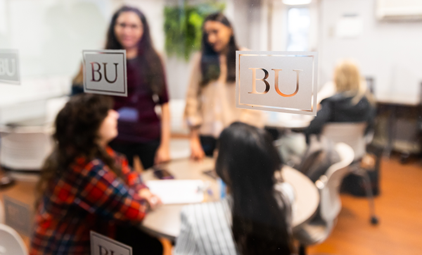 Students gather around a table, blurry behind glass