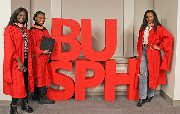 Three December 2022 grads stand with large red BUSPH letters