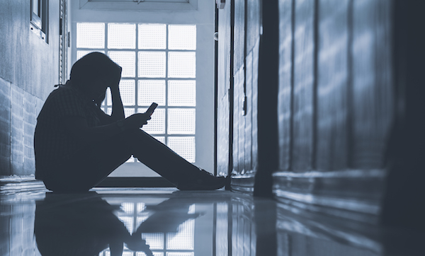 Woman sitting alone and looking smartphone with holding her head on corridor in front of room at apartment in low key style