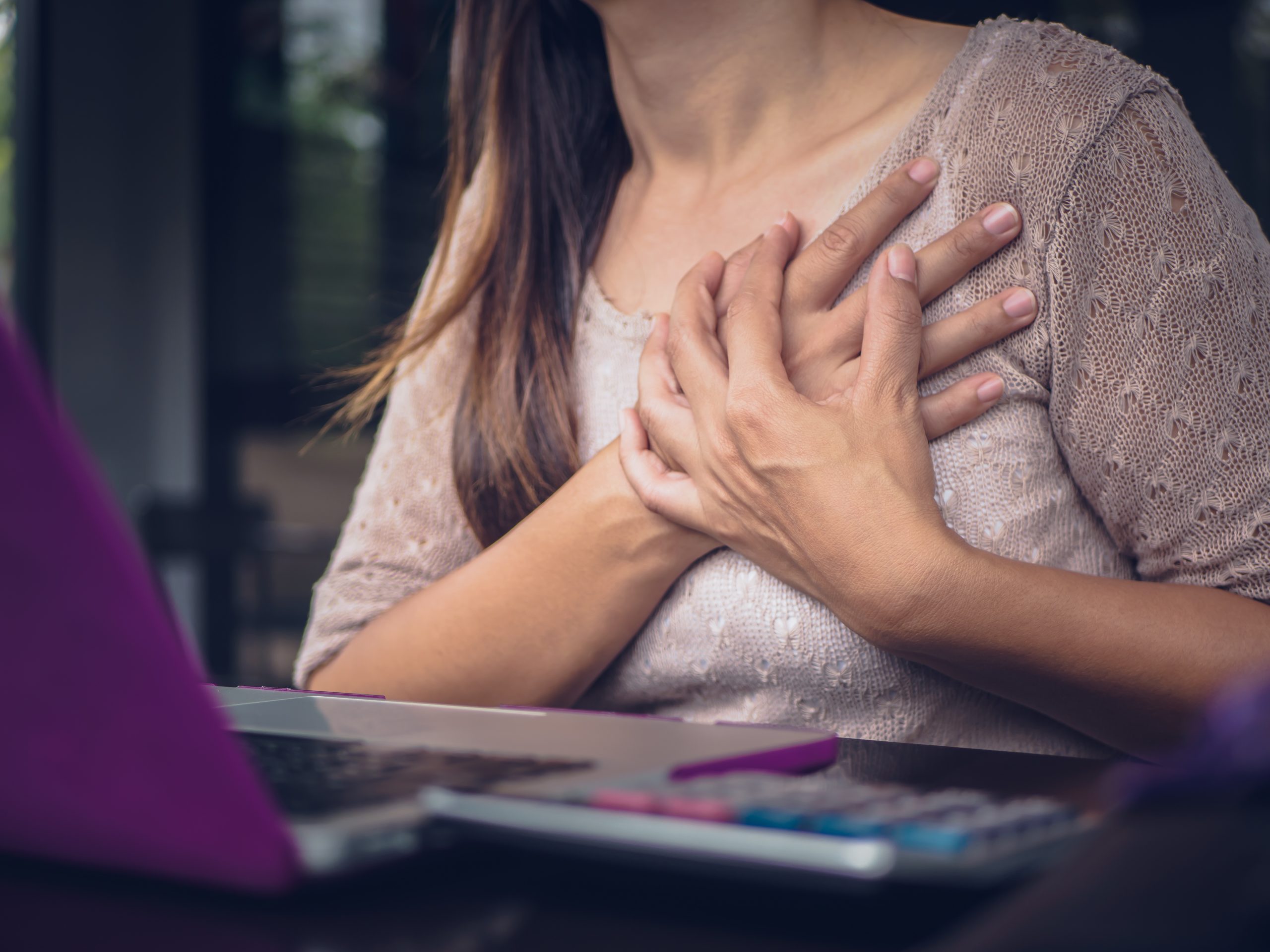 Woman touching breast and having chest pain after long hours work on computer. Office syndrome concept.