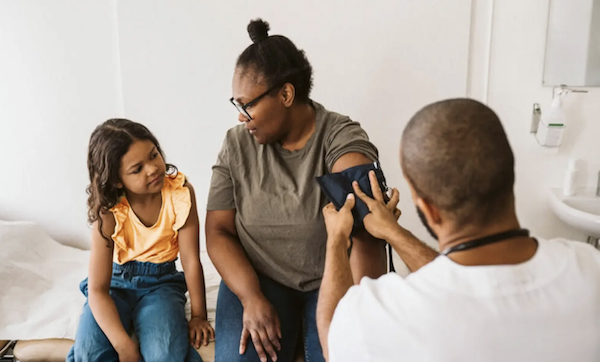 Nurse places blood pressure cuff on mother as her daughter watches