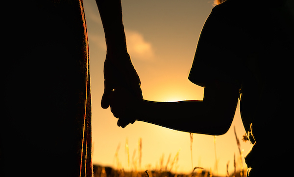 Silhouette of mother and child holding hands facing the sunset.