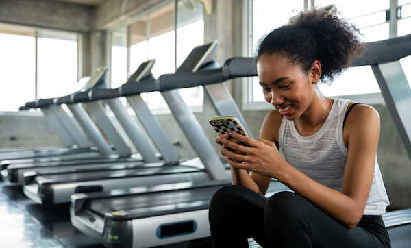 Athletic woman using mobile phone for social media or online shopping while workout exercise at fitness gym. Wellness female do sport training at sport club. Health care motivation concept.