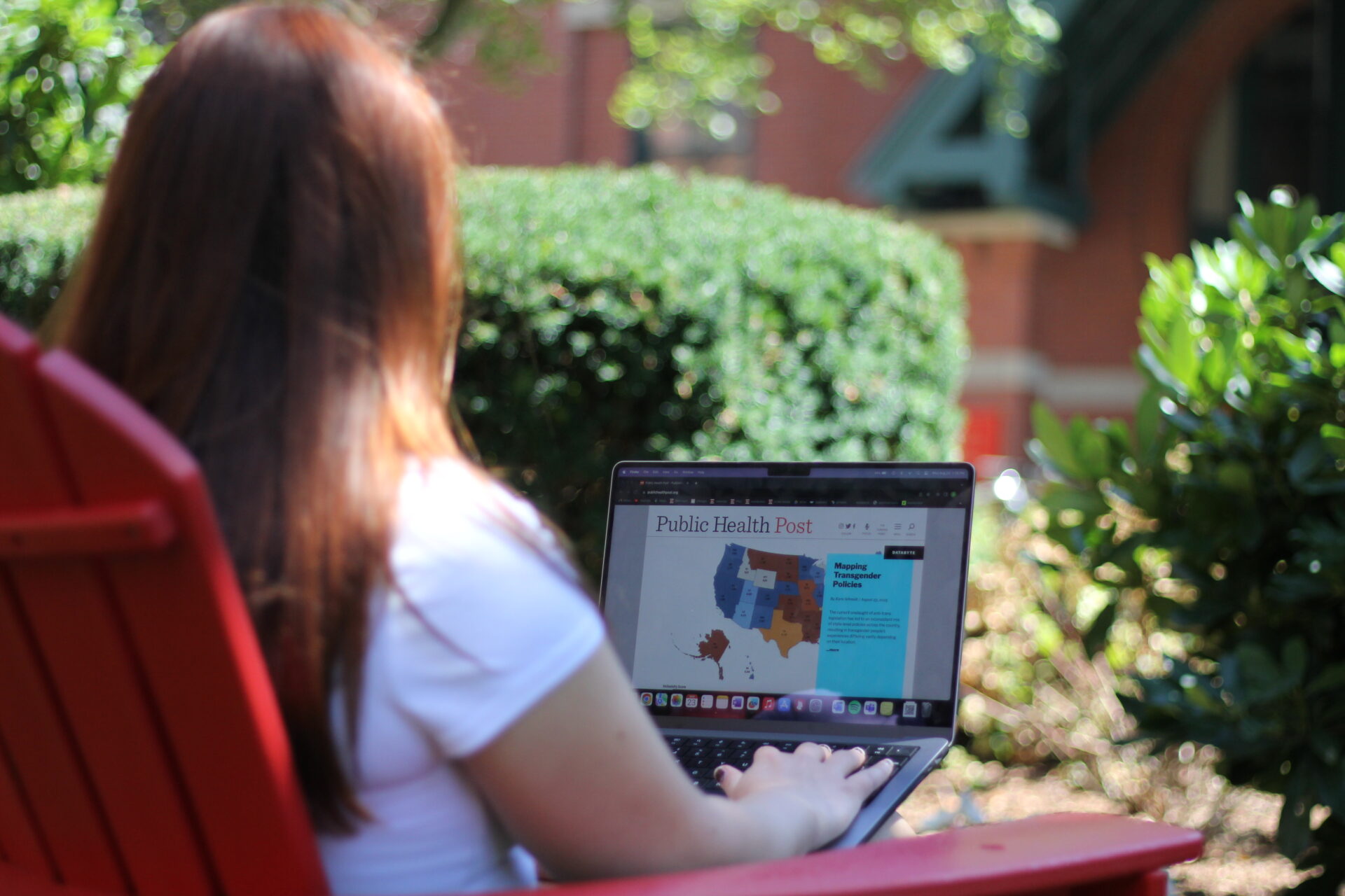A woman sitting in an adirondack chair in front of the Talbot Building looking at the PHP website on her laptop