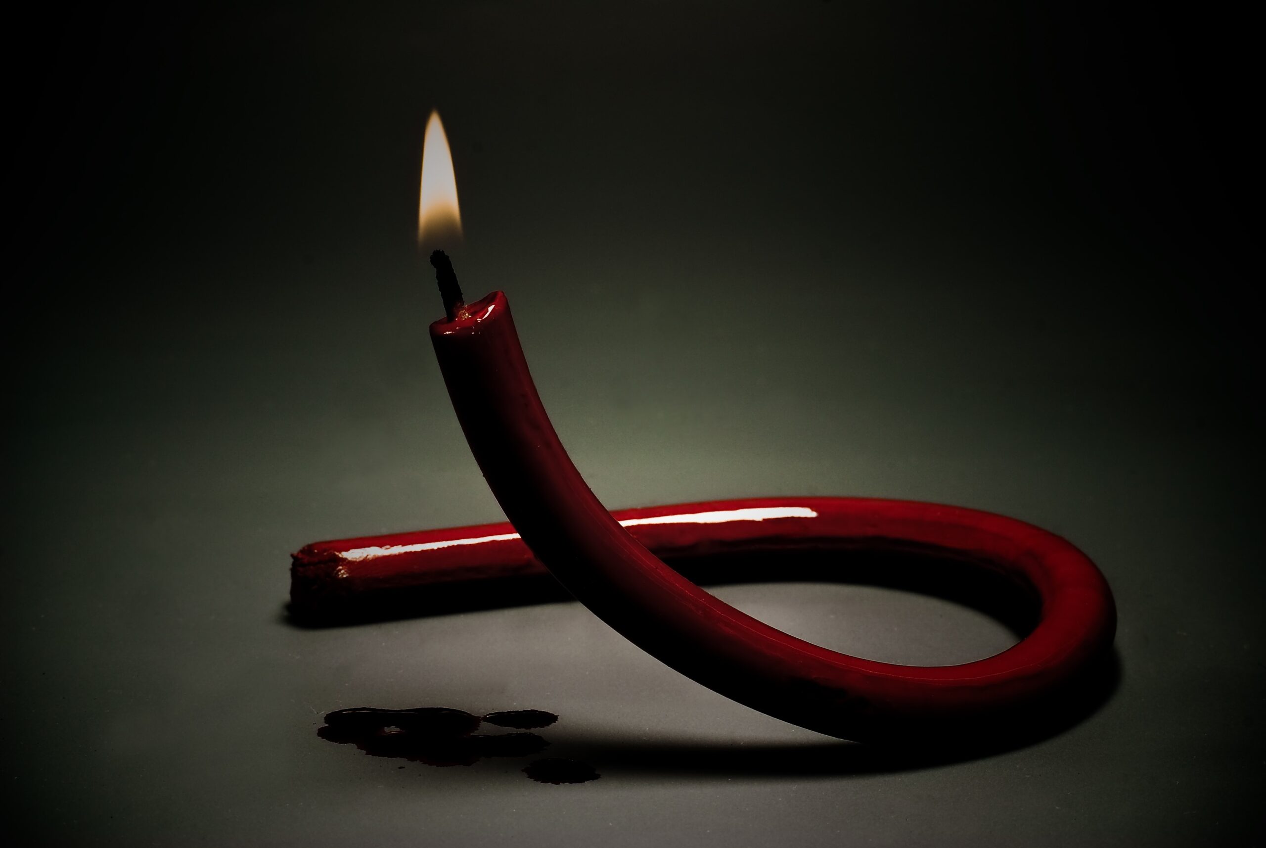 A lit candle in the shape of the red HIV/AIDS awareness ribbon