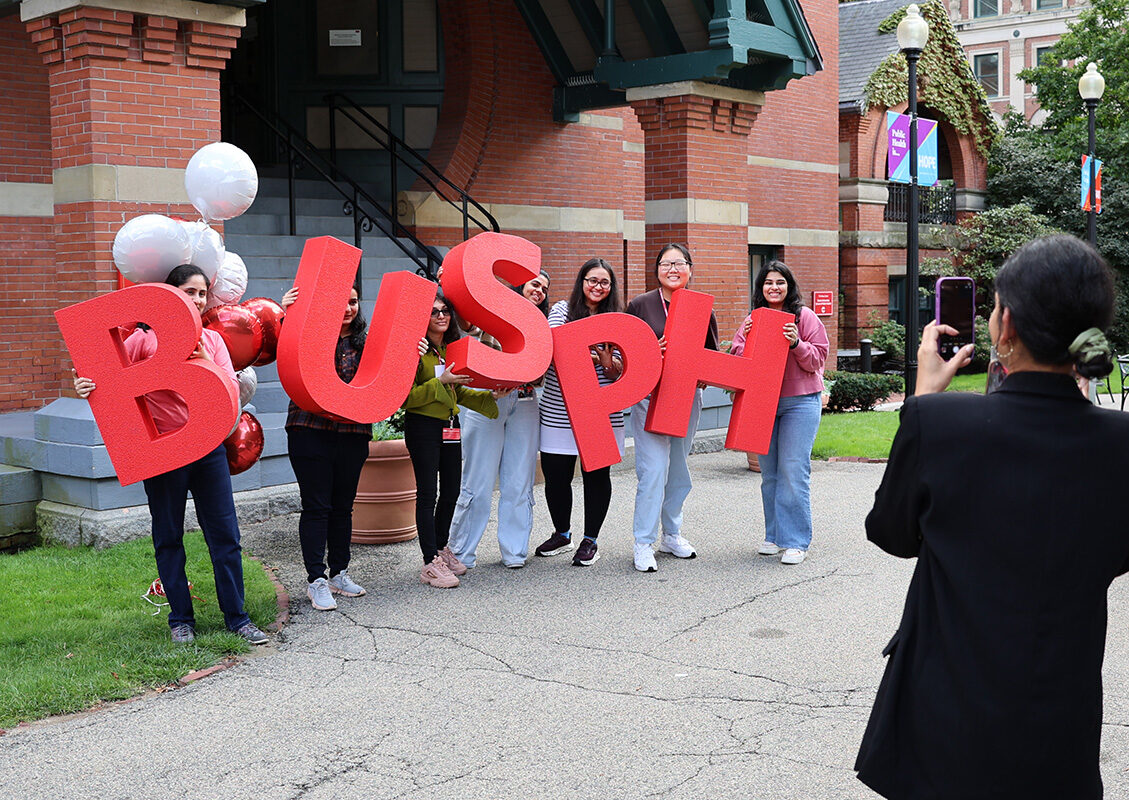 New students stand with large BUSPH letters in front of the Talbot building