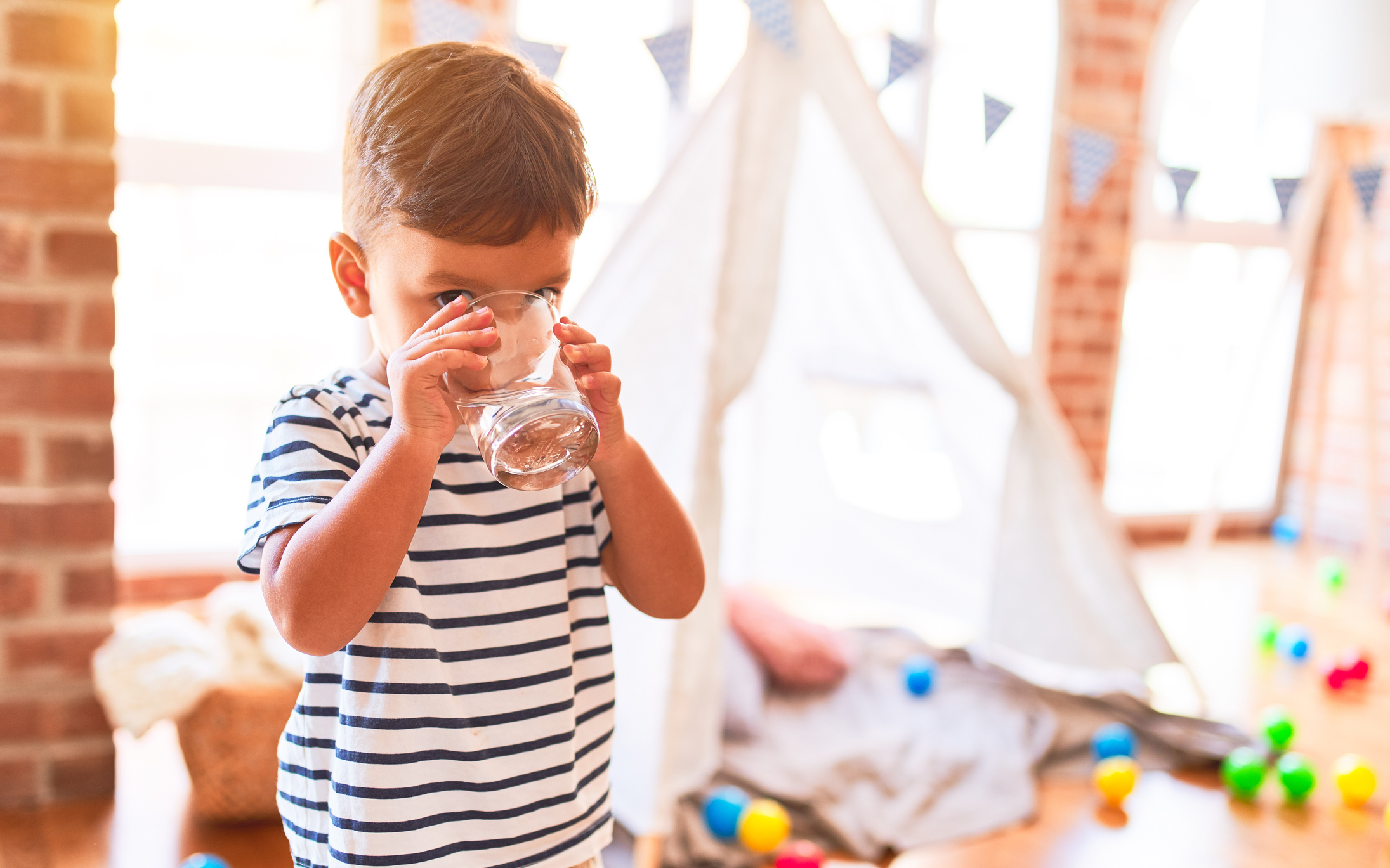 Toddler boy drinking glass of water at kindergarten