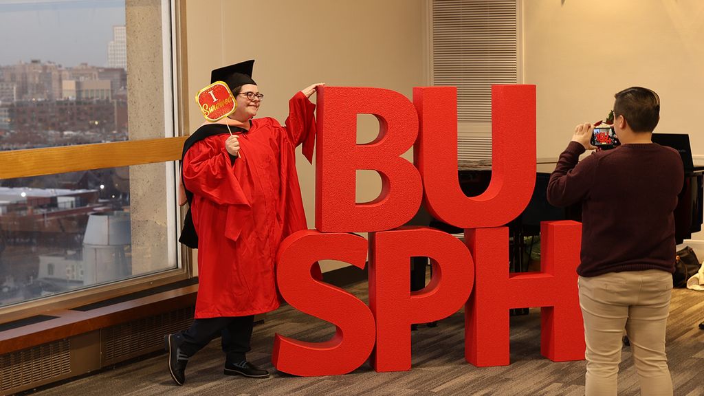 Recent grad celebrating at December ceremony beside BUSPH letters.