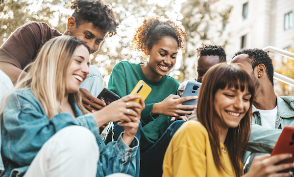 Happy university students watching cellphones sitting in college campus