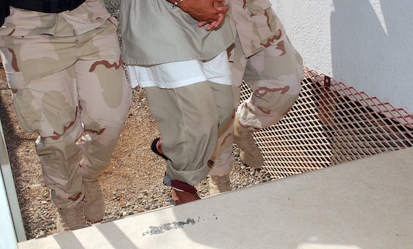 Guards prepare to escort a Guantanamo captive to the Camp Four medical facility. The guards and captive are visible only from the waist down.