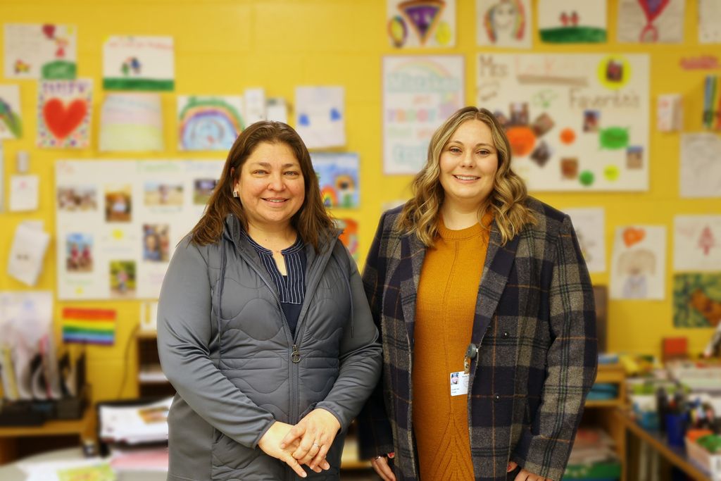 Patricia Fabian stands on the left and Katherine Walsh stands beside her on the right, they are in an elementary school classroom, the background is blurred