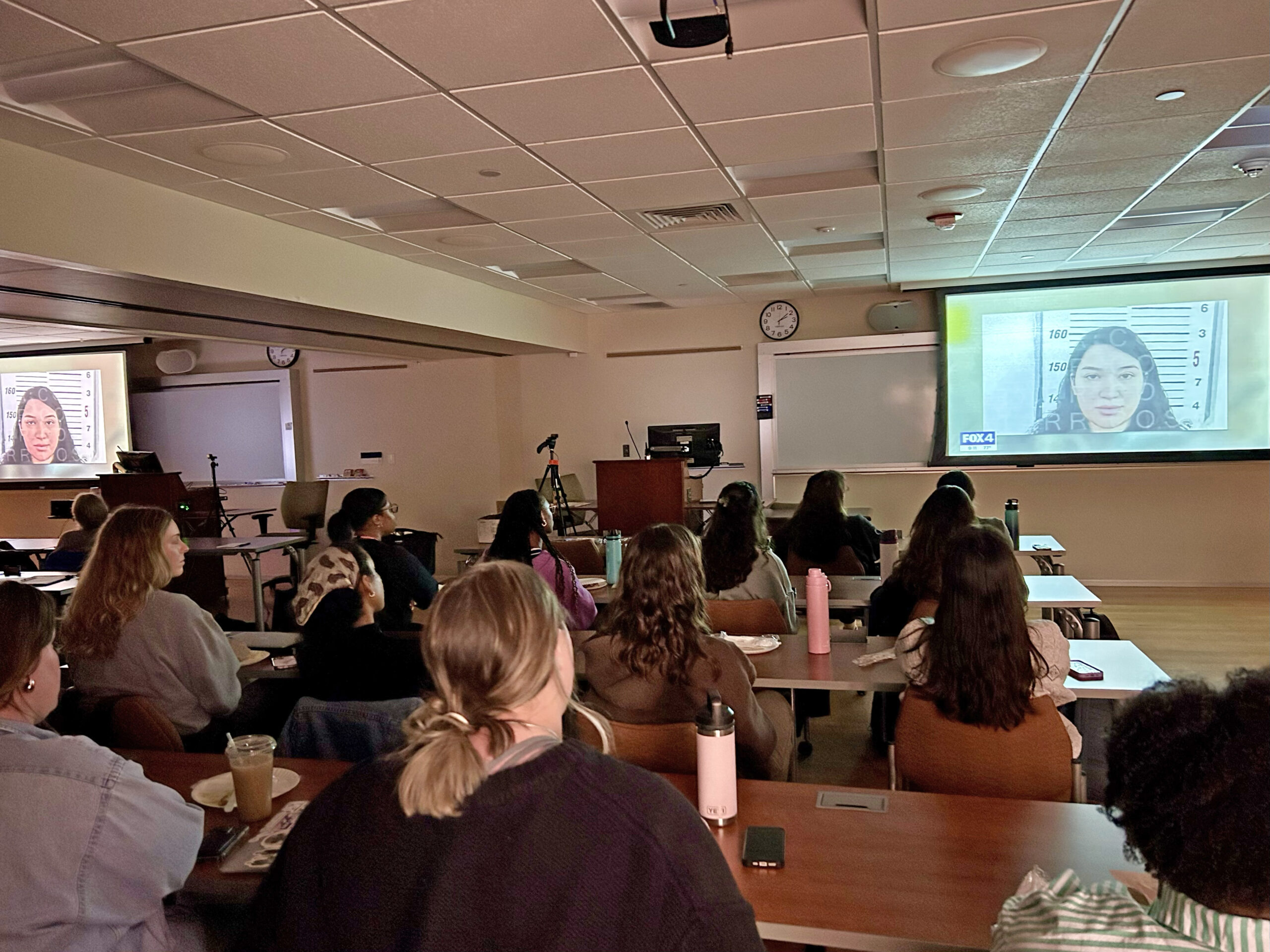 An audience looks on as the documentary Plan C plays on dual screens in a classroom