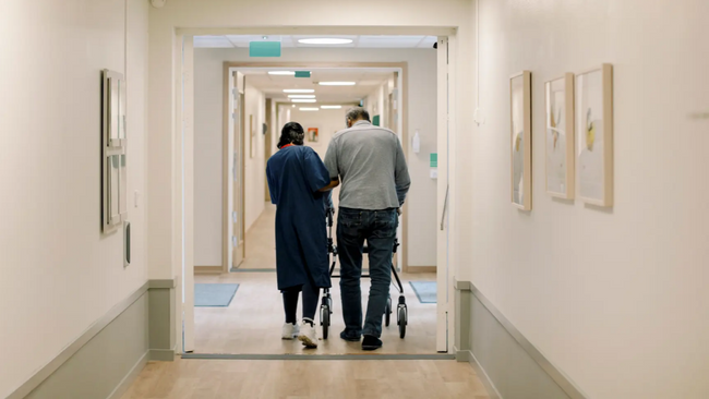 Nurse helping older man walk down hospital hallway