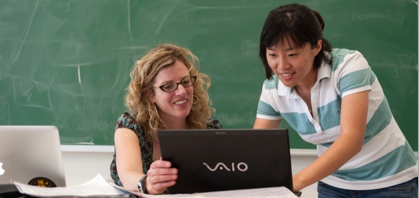 An instructor and one student confer at her desk with a laptop