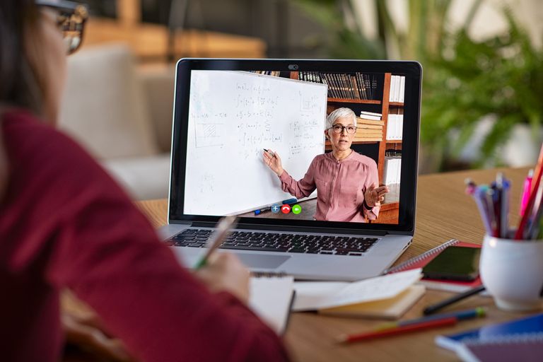 Person using a laptop to watch a person teaching with a whiteboard on a video conference