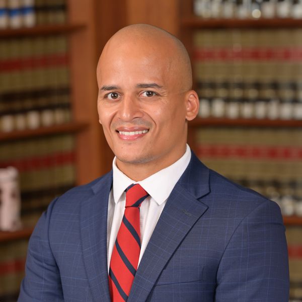 This is an image of Marcus. He is wearing a navy suit jacket with a white dress shirt and a red tie with navy blue stripes.