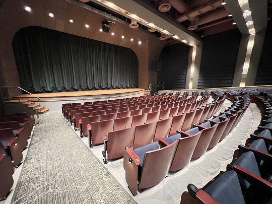 Angled view of stage with green curtain from the aisle of the house.