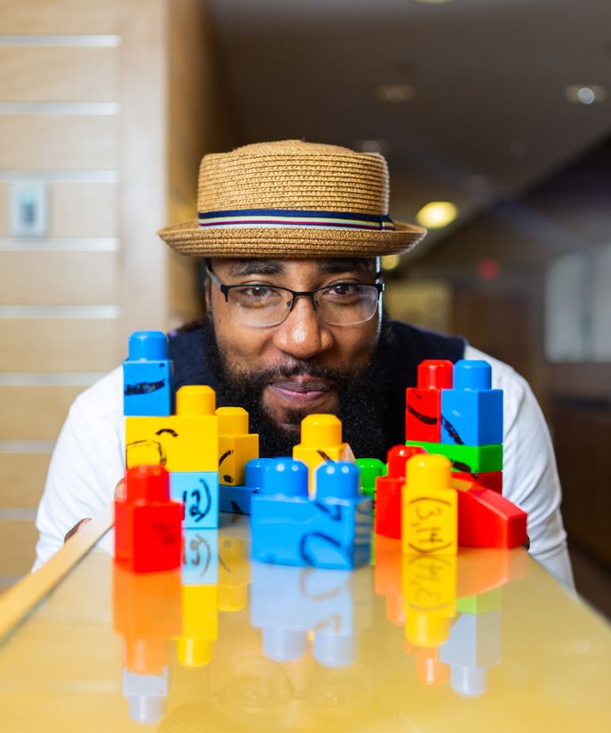 Greg Benoit sitting and smiling infront of children play blocks