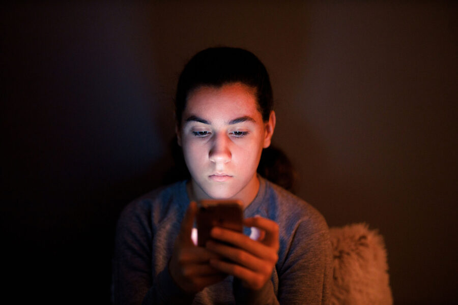 A teenage boy looking at his phone in a dimly lit room.