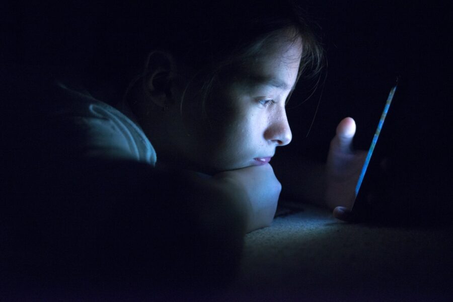 A child stares at his phone in a dimly lit room.