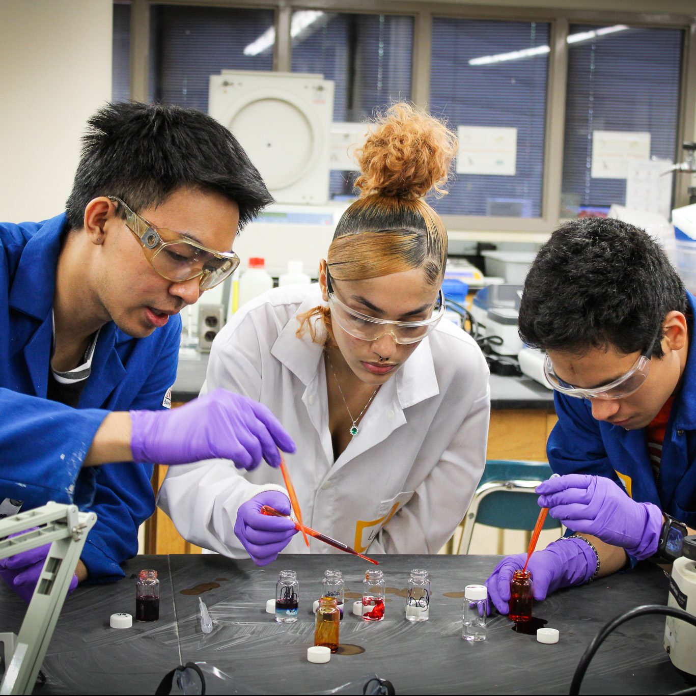 Three students work on a chemistry project with colored dye