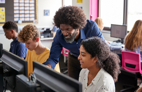 male teacher instructing middle school aged students working at computers