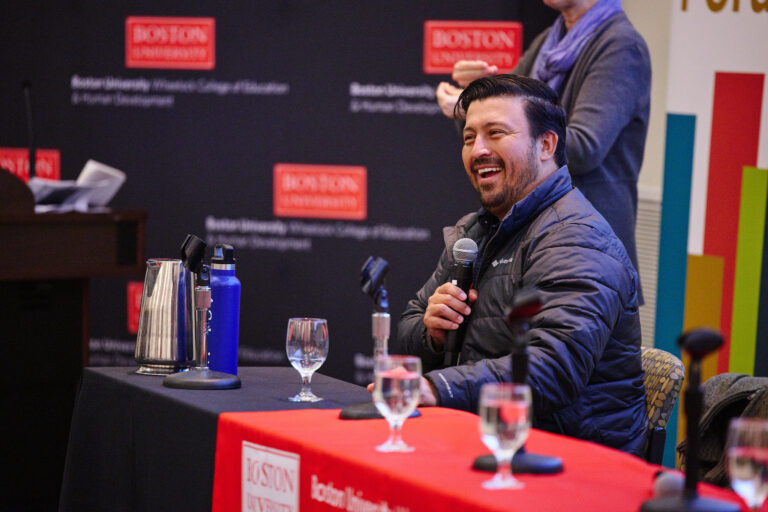 male speaker Oscar Gutierrez in jacket sitting at table smiling and talking into a microphone